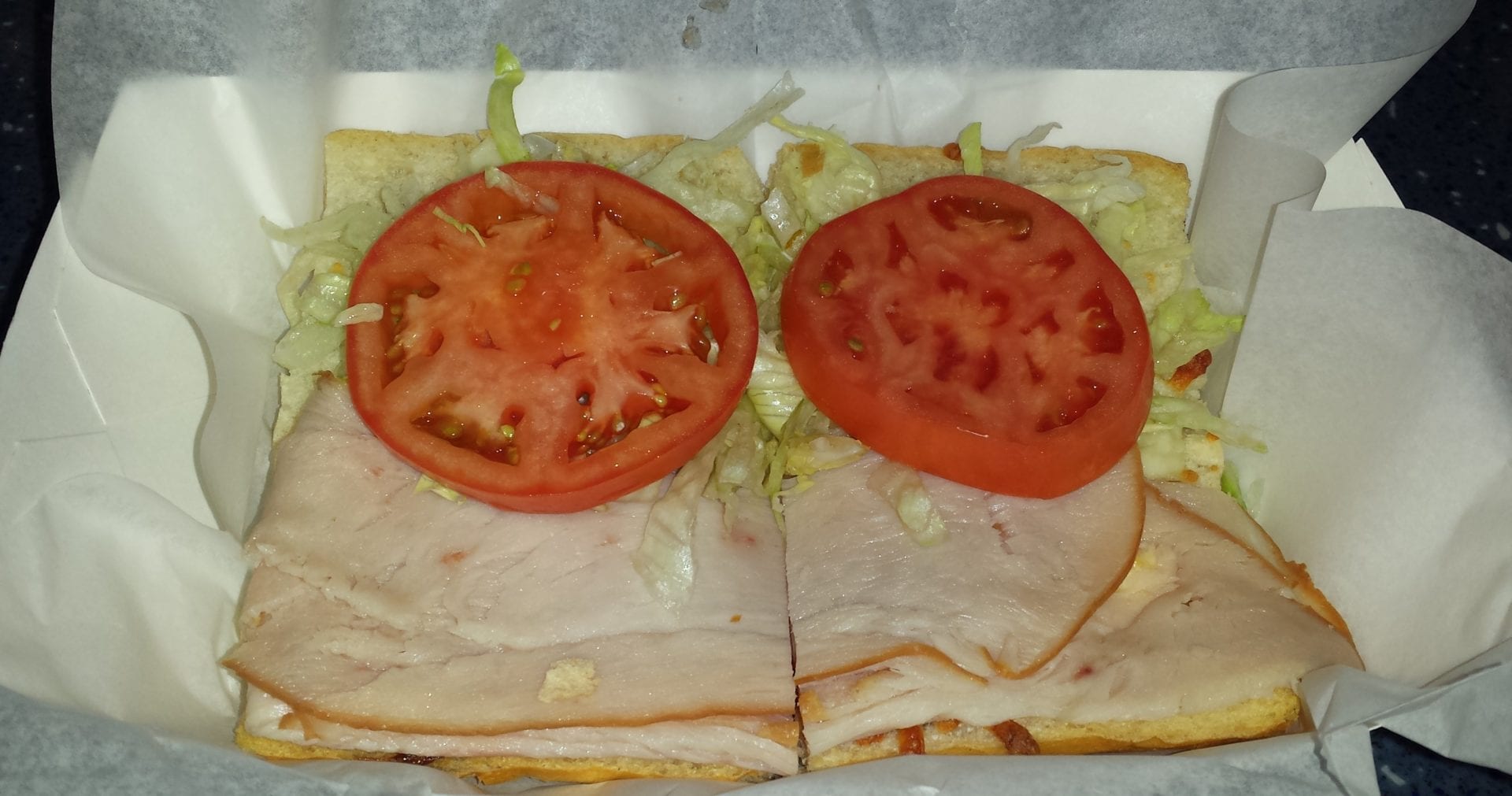 A sandwich cut in half with tomatoes on top.